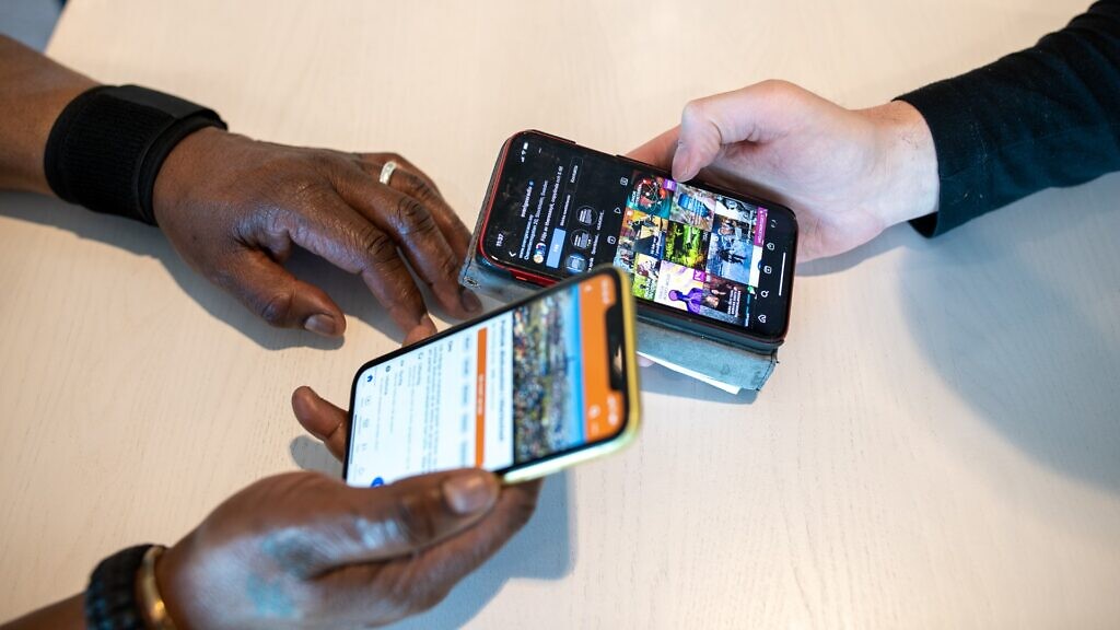 Två telefoner i motsatta riktningar hålls uppp av två armar över ett bord, den tredje armen ligger på bodet. Mobiltelefonerna är upplysta och visar två olika sidor.