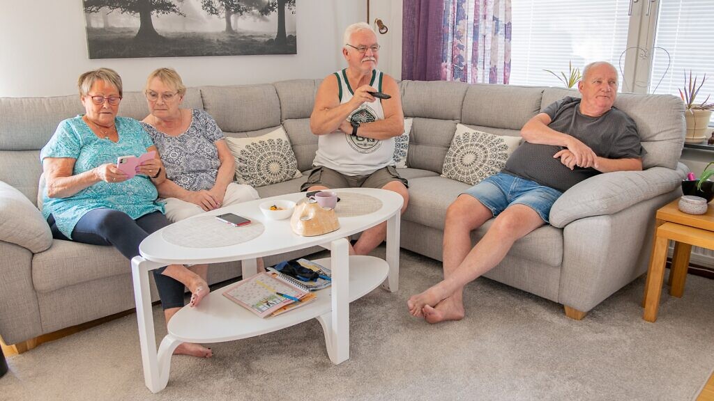 En grupp äldre människor som sitter på en soffa i ett vardagsrum.