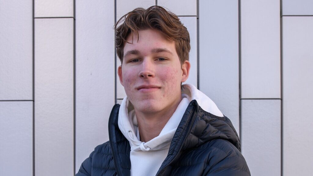 En man i puffig jacka lutar sig mot en vägg.