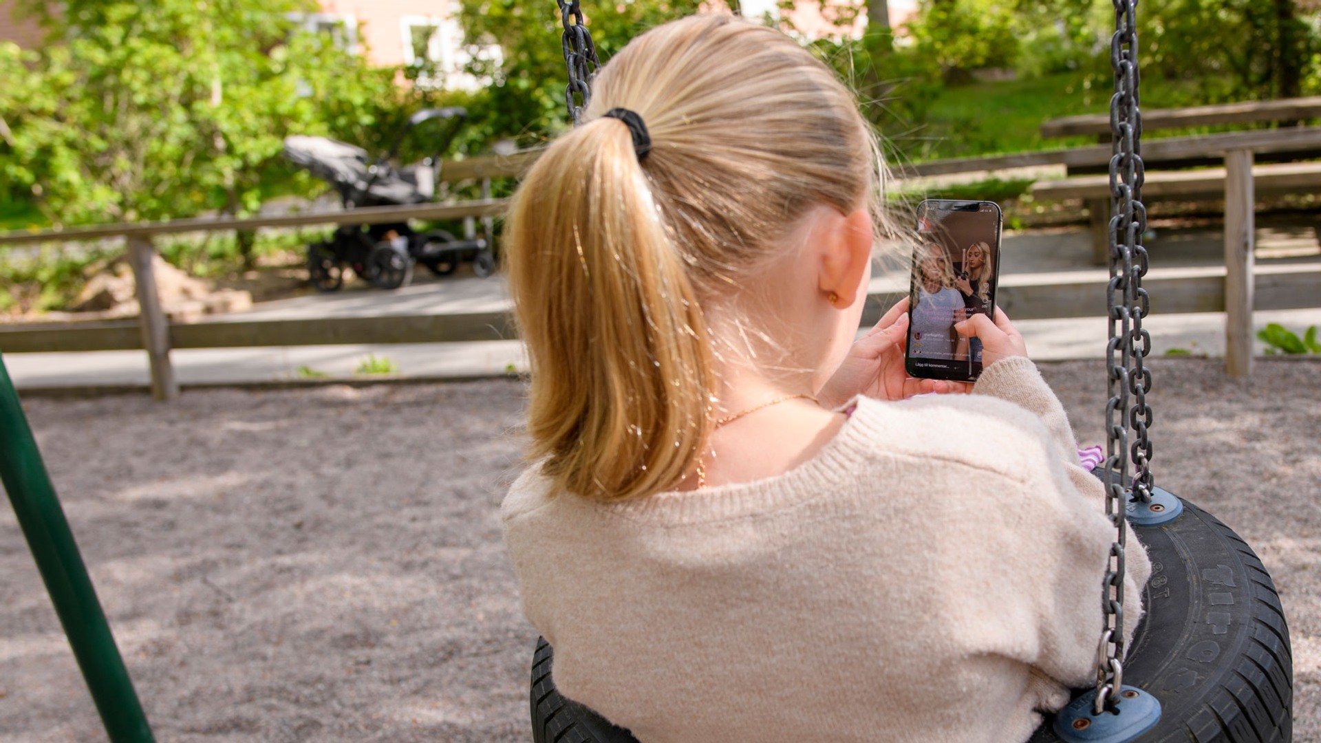 En flicka sitter i en gunga utomhus och tittar på sociala medier.