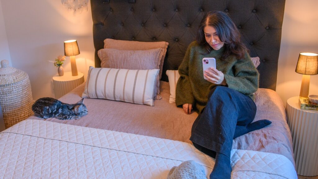 En kvinna sitter på en säng och legitimerar sig med FaceID mobiltelefon.