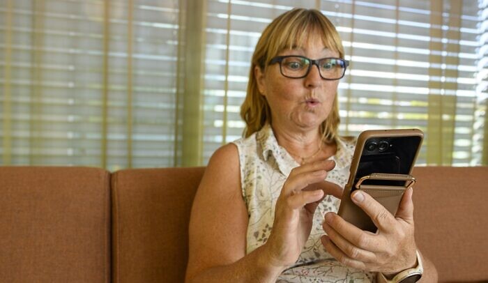 En kvinna sitter i en soffa och scrollar på mobilen.