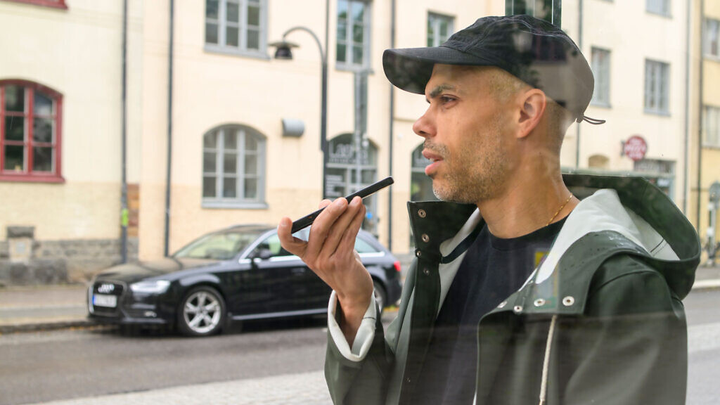 En man pratar med högtalarläge på mobilen i en busskur.