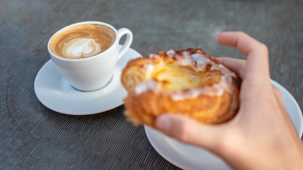 En person som håller en bakelse bredvid en kopp kaffe.