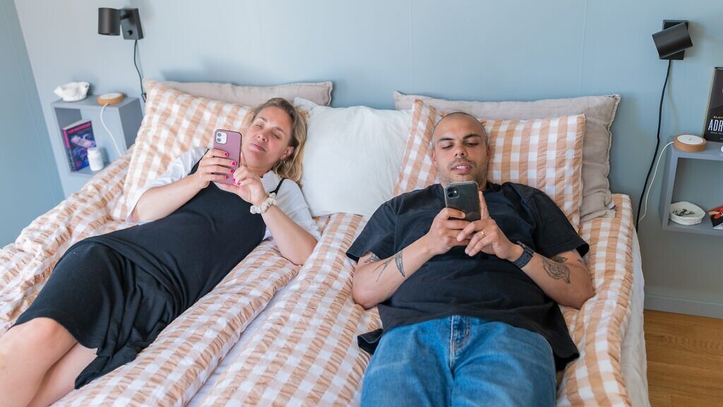 En man och en kvinna som ligger på en säng och tittar på en mobiltelefon.