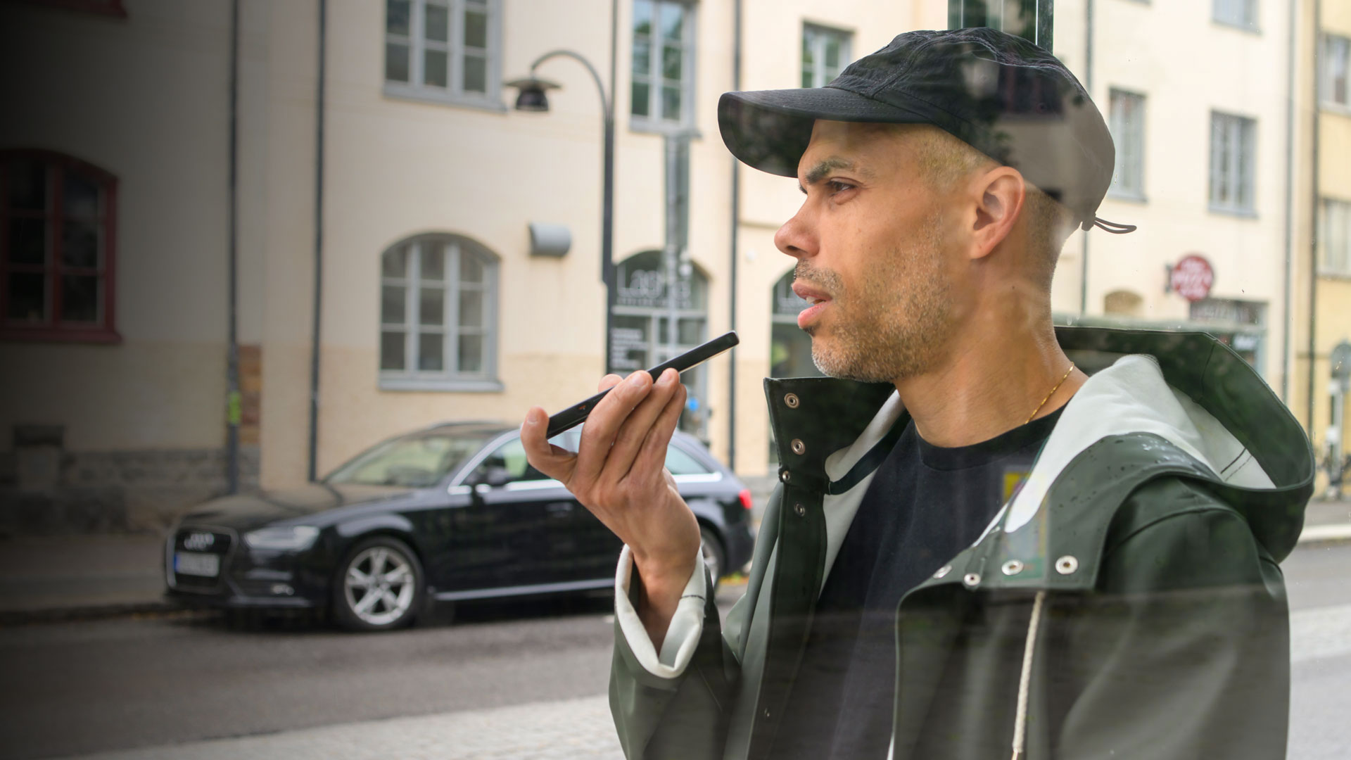 En man står vid en busskur och pratar i mobilen med högtalare på.