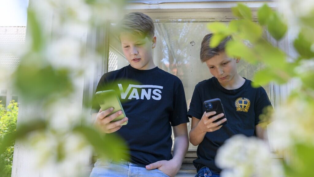 Två unga pojkar tittar på sina mobiltelefoner.