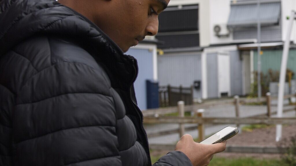 En man i svart jacka som tittar på sin mobiltelefon.